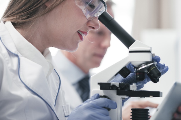 Female doctor analyzing under a microscope.